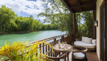 Fairmont Mayakoba gay-friendly hotel balcony view. Table with wine, chairs, and daybed overlook the lagoon. A relaxing gay travel destination.
