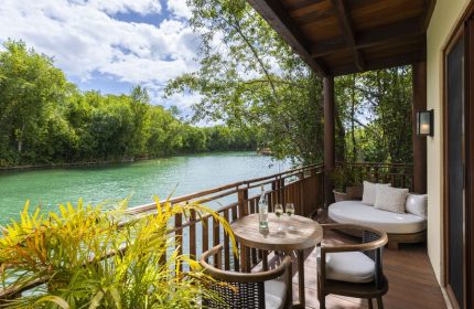 Fairmont Mayakoba gay-friendly hotel balcony view. Table with wine, chairs, and daybed overlook the lagoon. A relaxing gay travel destination.