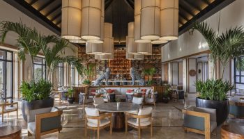 Fairmont Mayakoba's gay-friendly hotel interior. Lobby lounge with seating, bar, plants, and unique lighting. A luxury travel option for gay men.