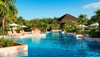 Fairmont Mayakoba's pool. This gay-friendly hotel offers luxury, sun loungers, umbrellas, and lush greenery. A perfect gay travel destination.