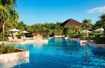 Fairmont Mayakoba's pool. This gay-friendly hotel offers luxury, sun loungers, umbrellas, and lush greenery. A perfect gay travel destination.