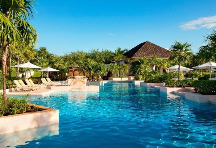Fairmont Mayakoba's pool. This gay-friendly hotel offers luxury, sun loungers, umbrellas, and lush greenery. A perfect gay travel destination.