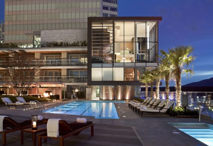 Fairmont Pacific Rim Hotel's outdoor pool at dusk. A gay-friendly hotel in Vancouver, BC, Canada. Palm trees and lounge chairs visible.
