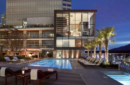 Fairmont Pacific Rim Hotel's outdoor pool at dusk. A gay-friendly hotel in Vancouver, BC, Canada. Palm trees and lounge chairs visible.