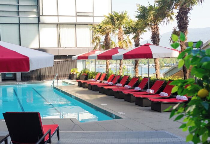 Fairmont Pacific Rim Hotel's pool area. Red lounge chairs line the pool, shaded by umbrellas. A gay-friendly hotel.