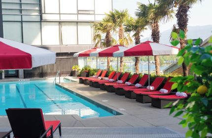 Fairmont Pacific Rim Hotel's pool area. Red lounge chairs line the pool, shaded by umbrellas. A gay-friendly hotel.