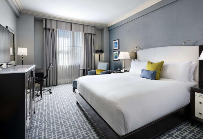 Gay-friendly Fairmont Royal York hotel room. King bed with white linens, desk, chair, and gray patterned carpet. Luxury gay travel.
