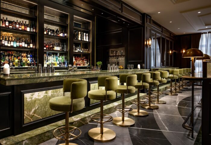 Gay-Friendly Hotel Fairmont Royal York bar. Olive green bar stools line the marble counter, bottles displayed on shelves behind.