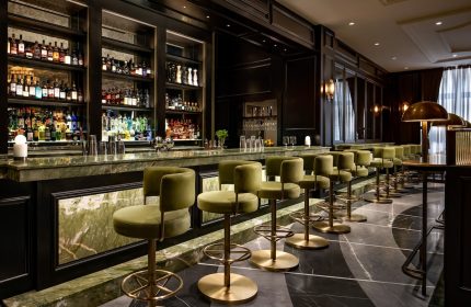 Gay-Friendly Hotel Fairmont Royal York bar. Olive green bar stools line the marble counter, bottles displayed on shelves behind.