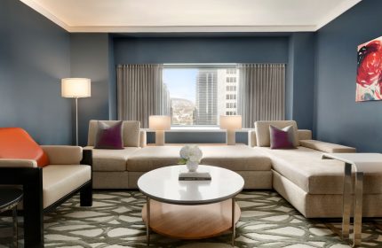 Fairmont The Queen Elizabeth hotel suite. Modern living room with sofa, chair, round table, and city view. Gay-friendly hotel interior.