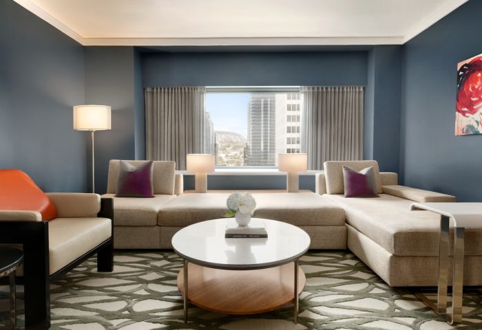 Fairmont The Queen Elizabeth hotel suite. Modern living room with sofa, chair, round table, and city view. Gay-friendly hotel interior.