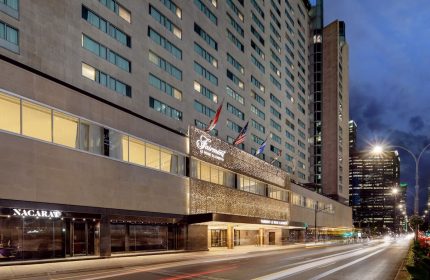 Fairmont The Queen Elizabeth, a gay-friendly hotel in Montreal. Exterior view at dusk with city lights and traffic. Upscale travel choice.