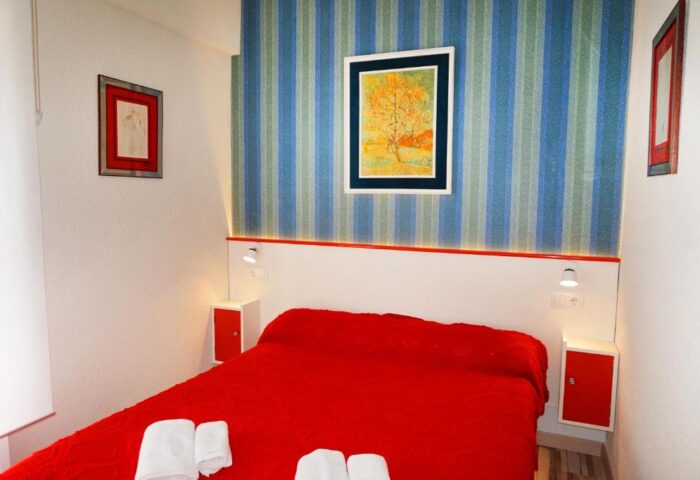 Far Home Gran Via gay-friendly hotel room. Red bedspread, striped wallpaper, and art. Gay travel lodging in Madrid, Spain.