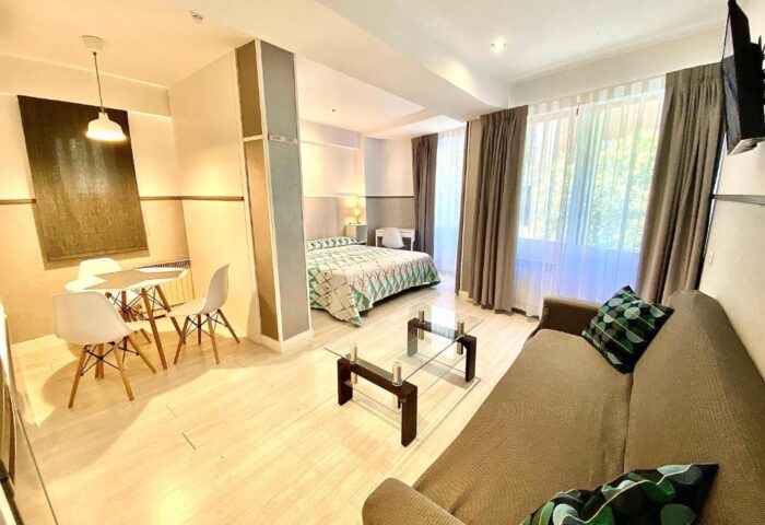 Far Home Gran Via gay-friendly hotel room. Living area with sofa, table, and chairs. Bedroom with bed. Modern design.