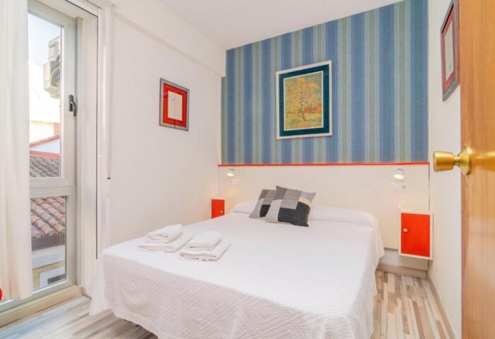 Far Home Gran Via gay-friendly hotel room. Double bed with white sheets, blue striped wallpaper, and a window. Ideal for gay travel.