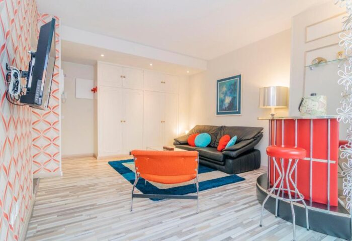 Far Home Gran Via gay-friendly hotel room. Living area with sofa, bar, TV, and colorful decor. Modern apartment interior.