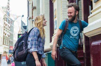 Gay-Friendly Flying Pigs Downtown Hostel Amsterdam entrance. Two travelers with backpacks enter the hostel. Budget travel in Amsterdam.