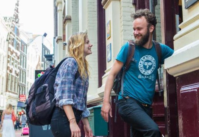 Gay-Friendly Flying Pigs Downtown Hostel Amsterdam entrance. Two travelers with backpacks enter the hostel. Budget travel in Amsterdam.