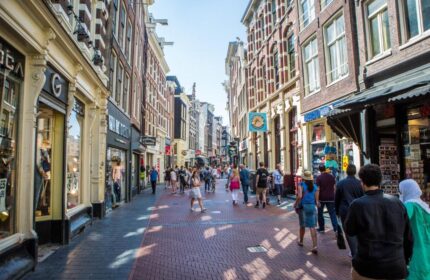 Amsterdam street scene near Flying Pigs Downtown Hostel. Gay-friendly hotel area with shops, red brick road, and many pedestrians.