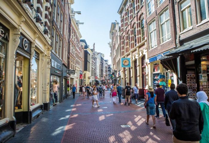 Amsterdam street scene near Flying Pigs Downtown Hostel. Gay-friendly hotel area with shops, red brick road, and many pedestrians.