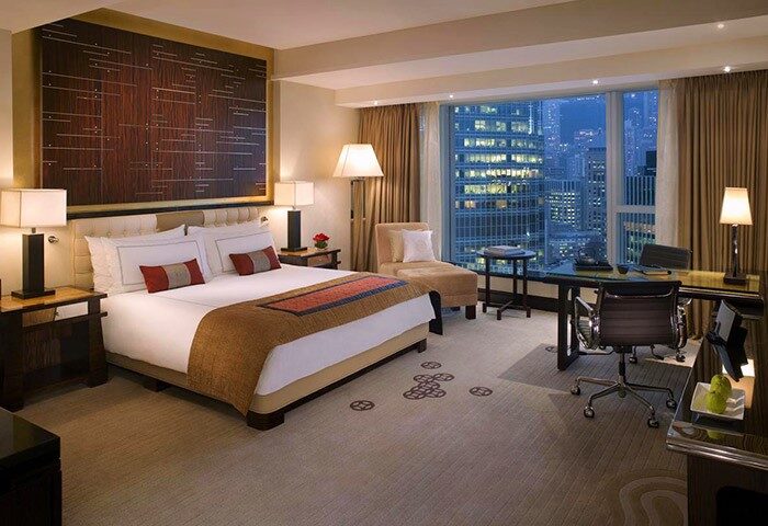 Four Seasons Hotel Hong Kong bedroom. Gay-friendly hotel with city views. Luxury travel for gay men. Stylish room, desk, and modern decor.
