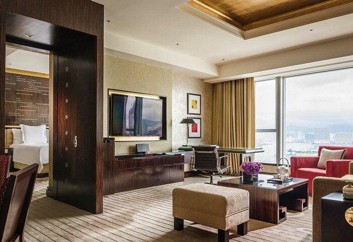 Four Seasons Hotel Hong Kong suite interior. Gay-friendly hotel room with city view, desk, TV, seating area, and luxurious design.