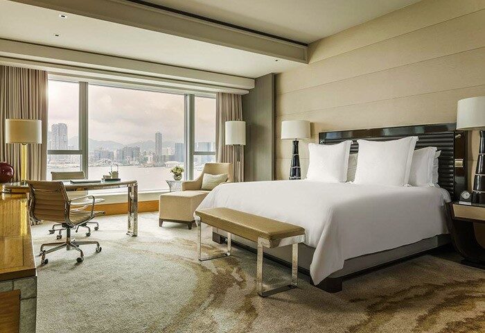 Four Seasons Hotel Hong Kong room. Gay-friendly hotel with a bed, desk, and city view. Luxury travel for gay men in Hong Kong.