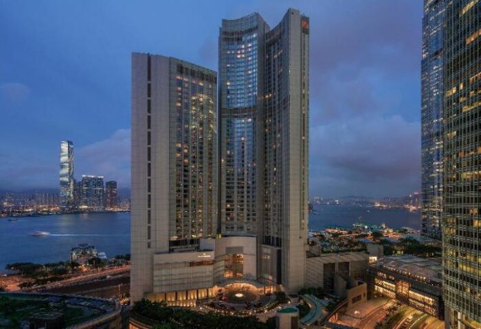 Four Seasons Hotel Hong Kong, a gay-friendly hotel. Night view of the luxury hotel with city skyline and harbor in the background.