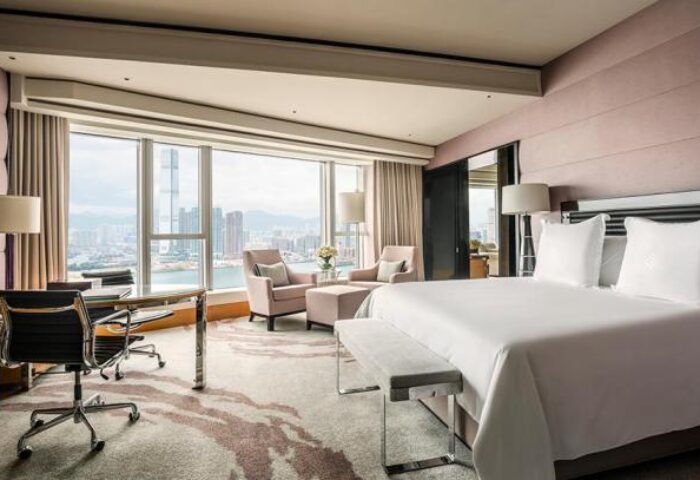 Four Seasons Hotel Hong Kong room. Gay-friendly hotel with city view. Bedroom with desk, chairs, and a large bed. Luxury travel.
