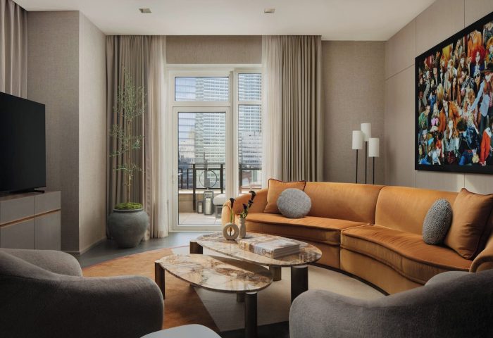 Four Seasons Hotel New York Downtown suite. Gay-friendly hotel with a living room, orange sofa, and balcony access. Upscale travel.