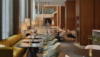 Four Seasons Hotel Toronto at Yorkville interior. Upscale lounge area with tables, chairs, and a staircase. A gay-friendly hotel.