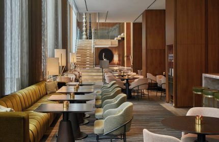 Four Seasons Hotel Toronto at Yorkville interior. Upscale lounge area with tables, chairs, and a staircase. A gay-friendly hotel.