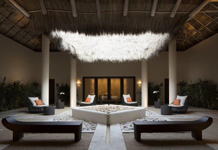 Courtyard at Gay-Friendly Four Seasons Resort Punta Mita. Thatched roof, seating, & pebble fountain create a serene, luxurious ambiance.