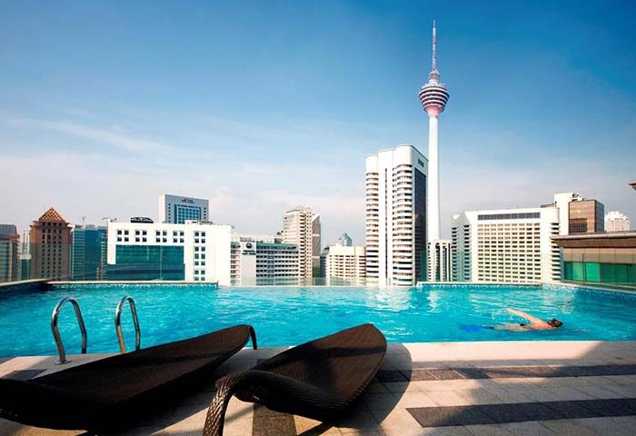 Rooftop pool at Fraser Place Kuala Lumpur, a gay-friendly hotel. Man swims with city skyline views. Ideal for gay travel in Kuala Lumpur.