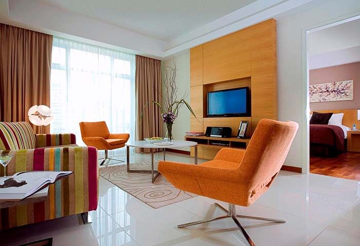 Fraser Place Kuala Lumpur suite. Living area with orange chairs, TV, and view into bedroom. Gay-friendly hotel for gay travel in Malaysia.