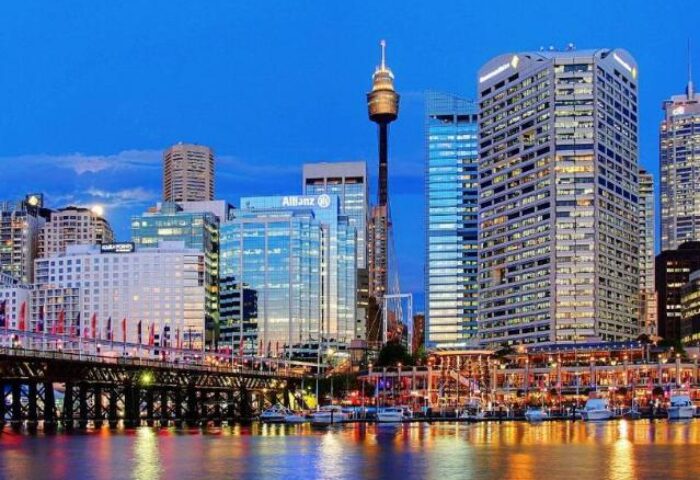 Sydney skyline at dusk. Fraser Suites Sydney, a gay-friendly hotel, reflected in the water. A vibrant choice for gay men travelers.