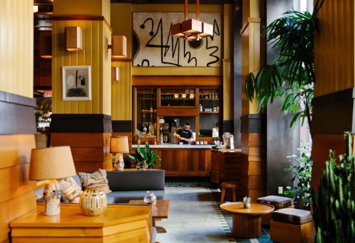 Freehand Los Angeles, a gay-friendly hotel. Lobby seating area with lamps, tables, plants, and a bar in the background. Stylish interior.