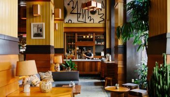 Freehand Los Angeles, a gay-friendly hotel. Lobby seating area with lamps, tables, plants, and a bar in the background. Stylish interior.