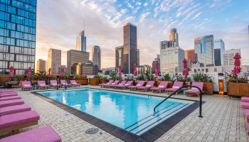 Rooftop pool at Freehand Los Angeles, a gay-friendly hotel. Pink lounge chairs line the pool, with the Los Angeles skyline in the background.