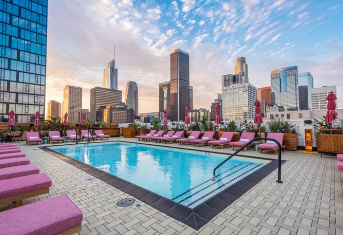 Rooftop pool at Freehand Los Angeles, a gay-friendly hotel. Pink lounge chairs line the pool, with the Los Angeles skyline in the background.