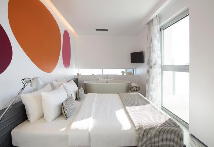 Fresh Hotel room interior: bed, tub, and colorful wall art. Modern gay-friendly hotel design with a spacious and bright atmosphere.