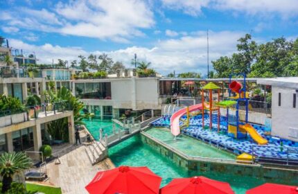 FuramaXclusive Ocean Beach Hotel Seminyak: Gay-friendly hotel with pool, kids' water park, and modern architecture under a blue sky.