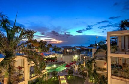 FuramaXclusive Ocean Beach Hotel Seminyak view at dusk. Gay-friendly hotel with pool, palm trees, and ocean view. Seminyak, Bali.