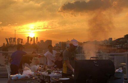 Sunset BBQ at G Guesthouse Itaewon in Seoul. Gay-friendly hotel rooftop view with men grilling, enjoying food, and the Seoul skyline.