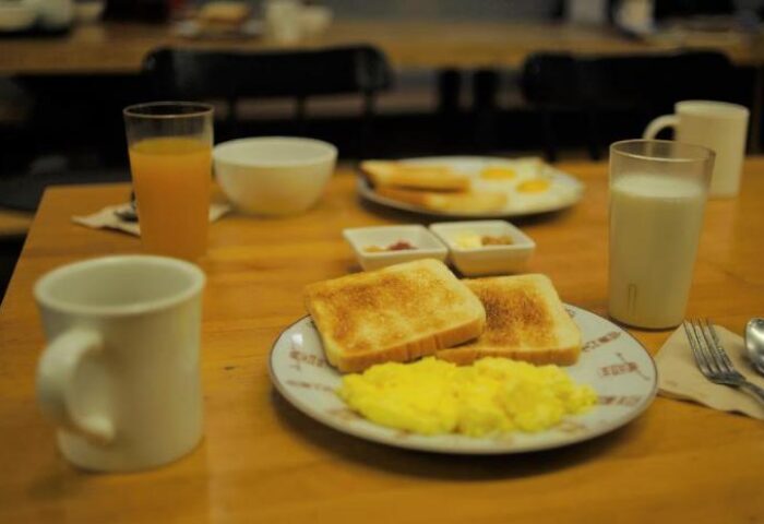 Breakfast at G Guesthouse Itaewon in Seoul, a gay-friendly hotel. Toast, scrambled eggs, juice, milk, and coffee on a wooden table.
