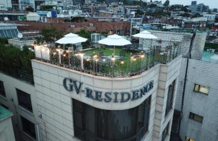 GV Residence, a gay-friendly hotel. Rooftop terrace with white umbrellas, lights, and seating. Urban setting. Ideal for gay men travel.