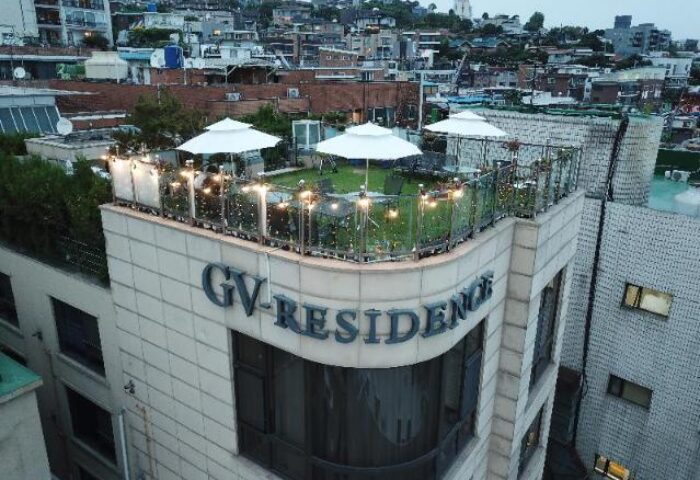 GV Residence, a gay-friendly hotel. Rooftop terrace with white umbrellas, lights, and seating. Urban setting. Ideal for gay men travel.