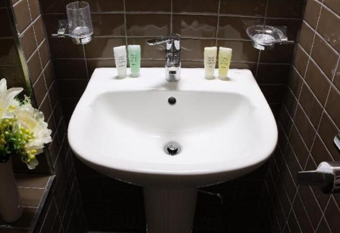 GV Residence gay-friendly hotel bathroom sink. Modern design, clean white basin, and brown tiled walls. Ideal for gay men's travel.