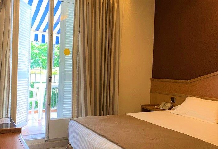 Galeon Gay-Friendly Hotel room featuring a balcony with blue and white striped awning. The room is decorated in neutral tones, creating a relaxing space.