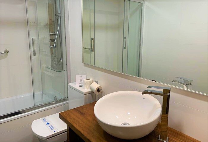 Galeon Gay-Friendly Hotel bathroom. Sink on wood counter, toilet with sanitary strip, shower with glass door, mirror. Gay travel advice.